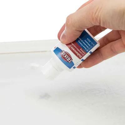Hånd holder tube med teksten 'TRIXIE Subeerin', væske presses ud på hvidt underlag. Synlig blå og rød etiket med produktnavn.