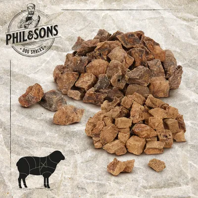 Phil & Sons koiranherkut. Kaksi kasaa kuivattuja lihapaloja, lampaan siluetti leikkauskuviolla. Phil & Sons koiranherkut. Kaksi kasaa kuivattuja lihapaloja, lampaan siluetti leikkauskuviolla.