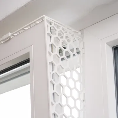 Bílé okenní ochranné mřížky s voštinovým vzorem, namontované na okenním rámu.