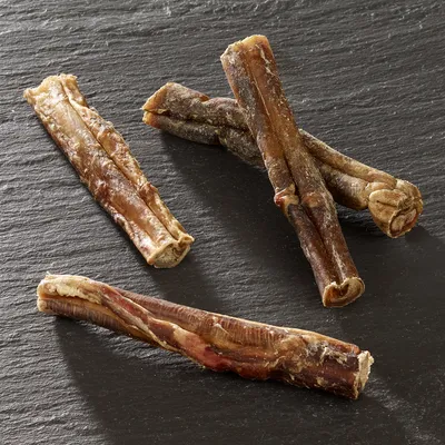 Vier getrocknete Kaustangen aus natürlichem Fleisch auf dunkler Oberfläche, geeignet als Snack für Haustiere.