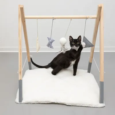 Lekbåge i trä med hängande tygleksaker, inklusive en svart kattunge på en vit matta.