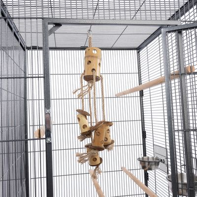Grande cage métallique avec perchoirs en bois, gamelles en acier inoxydable et jouet suspendu en bois et corde à l’intérieur.
