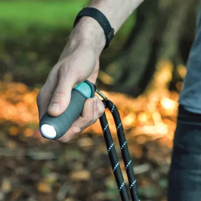 Hand hält eine graue Taschenlampe mit integrierter Hundeleinenbefestigung, geeignet für Spaziergänge bei Dunkelheit.