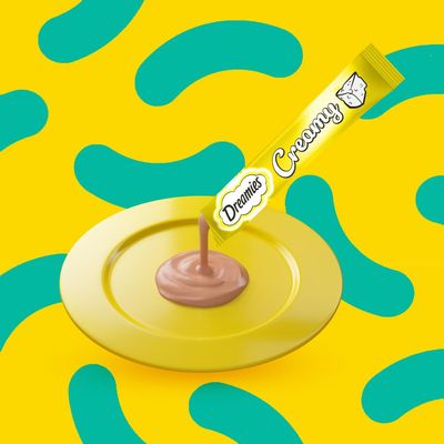 Creamy treat being squeezed from a Dreamies Creamy tube onto a yellow plate, showing product texture and serving suggestion.