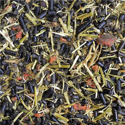 Close-up van voermix met zwarte pellets, gedroogde grassoorten en rode bestanddelen.