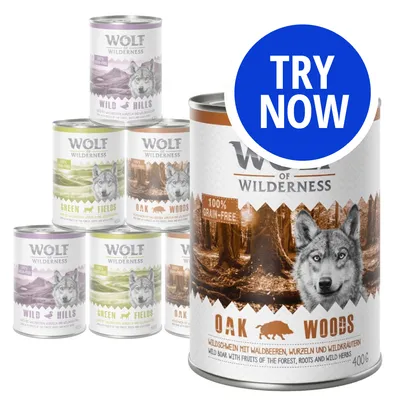 Selection of Wolf of Wilderness wet food cans with visible flavours including Wild Hills, Green Fields and Oak Woods. Large can shows 100% grain-free label and 'Try Now' callout.