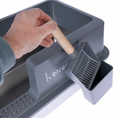 kooa kissanvessa harmaalla lapiolla ja puukahvalla, sisäänrakennettu jäteastia. Käsi pitää lapiota.