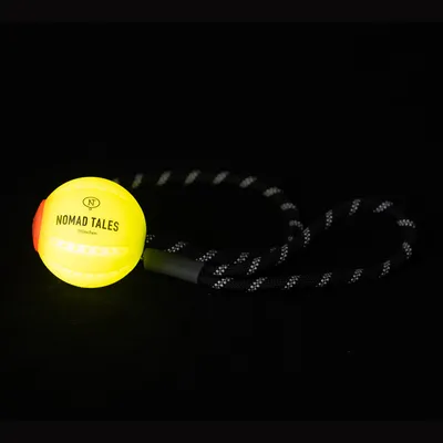Balle jaune avec inscription NOMAD TALES München, reliée à une corde noire à motifs blancs. Partie latérale orange visible sur la balle.