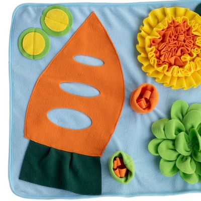 Snuffelmat van stof met kleurrijke elementen: oranje wortelvorm, gele bloem, groene cirkels en zakjes om traktaties te verstoppen.