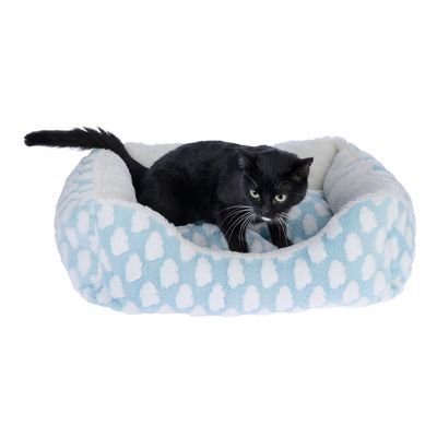 Gatto nero sdraiato in un letto per gatti azzurro chiaro con motivo a nuvole bianche e imbottitura morbida.