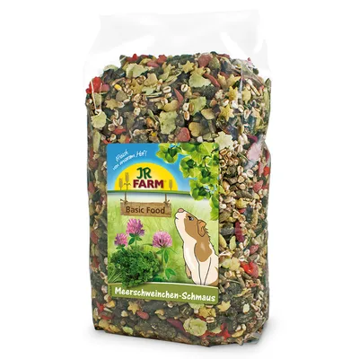 JR Farm Basic Food Meerschweinchen-Schmaus, genomskinlig plastpåse med blandat foder. Synlig etikett med illustration av marsvin och växter.