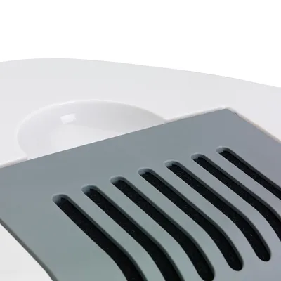 Gros plan sur une surface en plastique blanc avec un couvercle gris comportant des fentes allongées. Aucun texte ou marque visible.