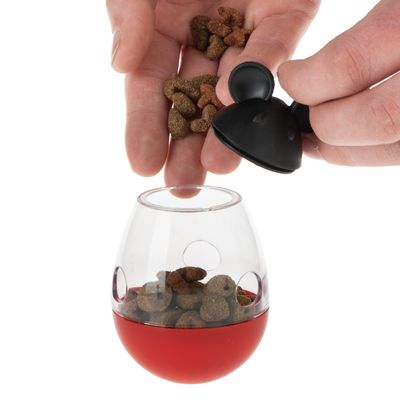 Main tenant un distributeur transparent avec base rouge contenant des croquettes pour animaux. Partie supérieure de l’objet masquée.