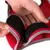 Close-up of hands demonstrating how to fasten a red harness using a black hook and loop (Velcro) strap.