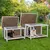 Deux niches pour chiens en bois avec cadre blanc, toits ouverts, un chien noir dans la petite niche et un chien blanc et noir dans la grande niche, posées sur une pelouse de jardin.