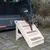 Hund steigt eine beige Kunststoff-Haustiertreppe mit Teppichstufen hinab, die an einem geöffneten Kofferraum eines Autos positioniert ist.