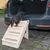 Hund steigt eine beige Kunststoff-Haustiertreppe hinunter, die an den Kofferraum eines Autos führt. Treppe mit vier Stufen und rutschfester Oberfläche.