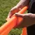Hand befestigt ein orangefarbenes Klettband an einer gerippten Kunststoffstange, geeignet für den Aufbau von Trainings- oder Spielgeräten.