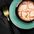 Bowl with white fish in sauce, served on a green plate. Golden fork and black cloth beside it.