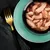 Close-up of shredded chicken in sauce, served in a black bowl on a green plate with a gold fork next to it.