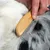 Hand hält einen Holzkamm mit Metallzinken, der durch das Fell eines schwarz-weissen Tieres gleitet.