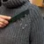 Hand verwendet grüne Bürste, um Tierhaare von einem grauen Wollpullover zu entfernen.