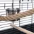 Close-up view of a cage accessory with stainless steel bowl, sisal rope and wooden perch attached to a metal grid.
