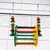 Brinquedo suspenso de madeira colorida para gaiolas, com barras horizontais e contas redondas multicoloridas, pendurado por correntes metálicas.