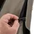 Close-up van een hand die een zwarte sluiting op een bruine stof met netmateriaal opent of sluit.