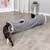 Grauer Katzentunnel mit zwei Öffnungen und Plüschrand, eine Katze spielt am Eingang, eine andere schaut aus der mittleren Öffnung heraus.