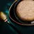 Close-up of a bowl with shredded wet food, beige colour, served on a dark plate. Golden spoon next to it.