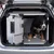 Dog sitting in a silver transport box with metal grid door in the boot of a car. Box made of aluminium and plastic, suitable for safe transport.