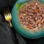 Chunks of meat in gravy with small pieces of carrot and potato served on a green plate, garnished with fresh basil.