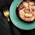 Close-up of a bowl with wet food, visible shrimp and chicken pieces in sauce, served on a green plate with a golden fork.