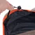 Gros plan sur une main ajustant un cordon élastique noir avec bloqueur sur le bord d’un tissu intérieur noir à liseré orange, extérieur en tissu marron.