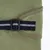 Détail d’une sangle noire avec bande réfléchissante et boucle en plastique sur tissu vert, couture visible. Matériaux : tissu synthétique, plastique.