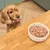 Dog looking at a bowl of wet pet food on a wooden table, demonstrating product use during mealtime.
