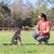 Una persona mostra un gioco verde a un cane e tiene una confezione di snack in mano durante l’addestramento all’aperto.