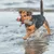 Hund spielt im Wasser und trägt ein rotes und graues Spielzeug mit integriertem Behälter.