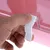 Hand zeigt, wie ein weisser Verschluss an einer rosa Box geöffnet wird.