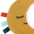 Crescent-shaped fabric toy in yellow with embroidered face and coloured ribbons: red, turquoise, dark green. Made of fabric and plush.