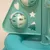 Jouet pour chat en plastique turquoise avec balles ajourées et découpes en forme de cœur, étoile et sapin visibles sur la structure.