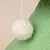 Zawieszona zabawka z białego, puszystego materiału na sznurku na zielonym tle.