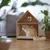 Wooden house with window and door, suitable as a retreat for pets. Beige cat sitting on a padded cushion inside the house.