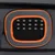 Détail d’une fenêtre en maille noire avec bordure orange sur un sac ou une caisse de transport gris, fermeture éclair visible à gauche.