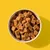 Bowl filled with brown, cube-shaped pet food or treats displayed on a yellow background.