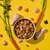 Bowl of cubed pet food surrounded by raw chicken pieces, carrots, grains, and herbs, showing visible ingredients used in the product.