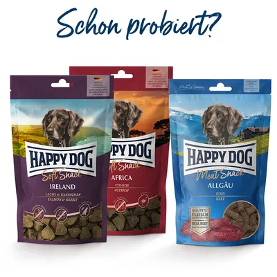 Trois sachets de friandises pour chien Happy Dog : Soft Snack Ireland (saumon et lapin), Soft Snack Africa (autruche), Meat Snack Allgäu (bœuf). Textes en allemand visibles sur les emballages.