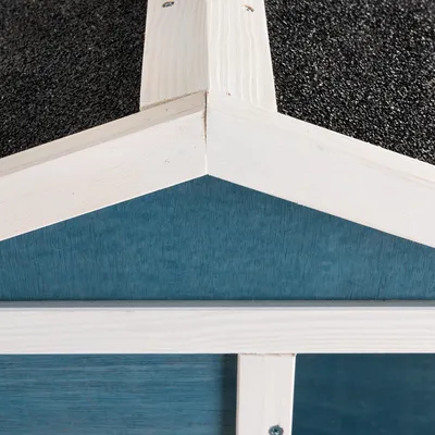 Detailansicht eines blauen Holzhauses mit weissem Rahmen und schwarzem Dach aus rauem Material.