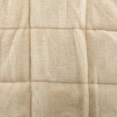 Detalle de tejido beige con textura suave y costuras visibles en forma de cuadros. Material tipo felpa o forro polar.